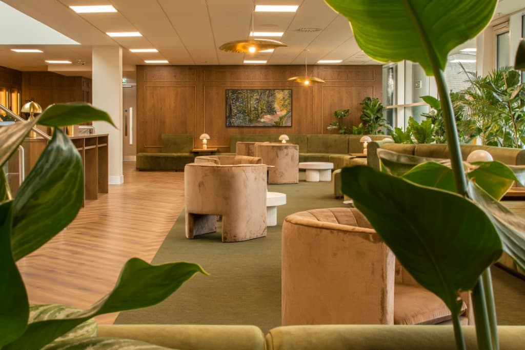 Modern lounge with warm wood paneling, olive seating, and indoor plants